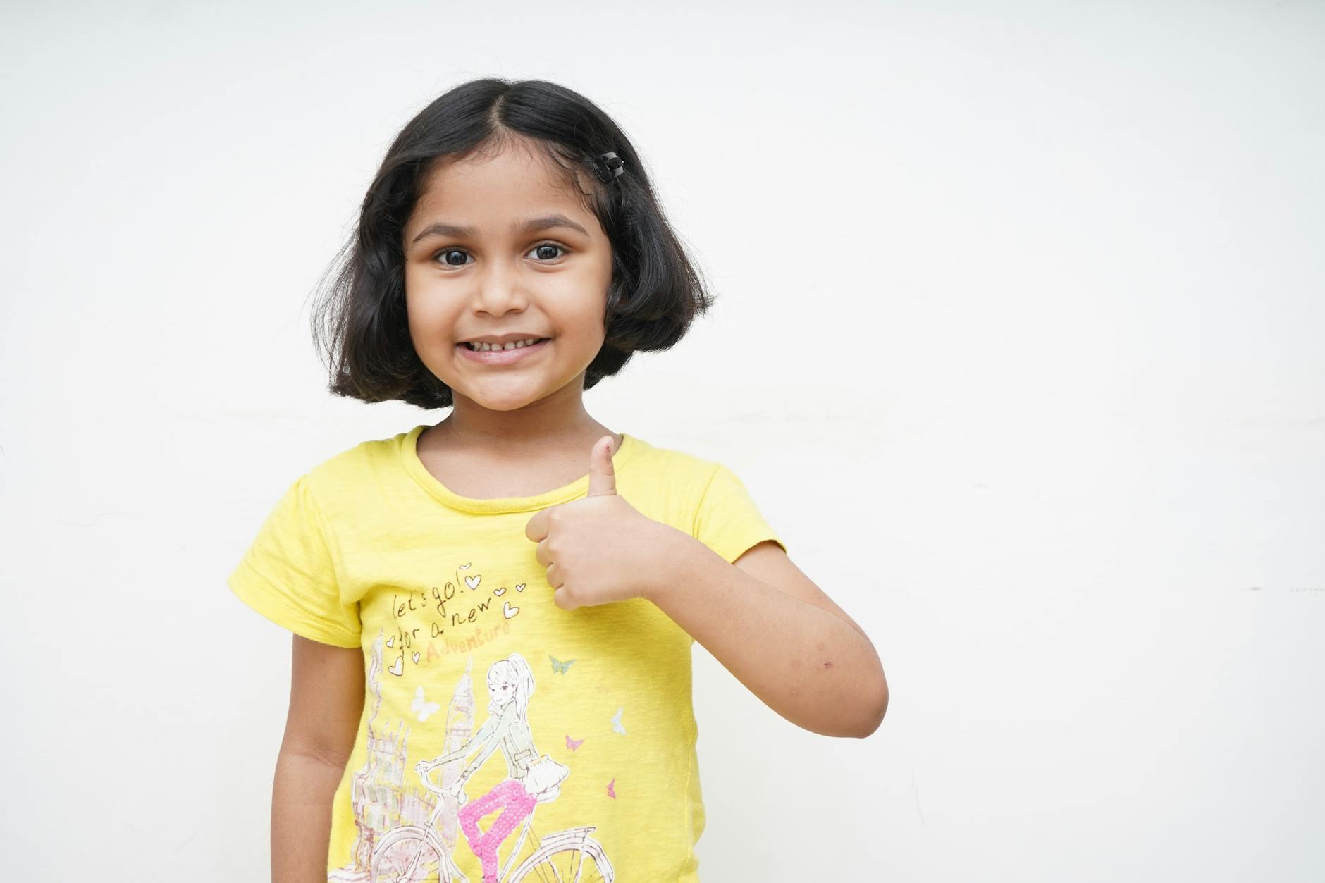 a smiling little girl doing a thumbs up
